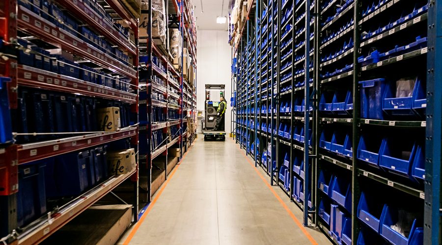 Warehouse aisle with shelving units stocked with blue bins and a forklift operator